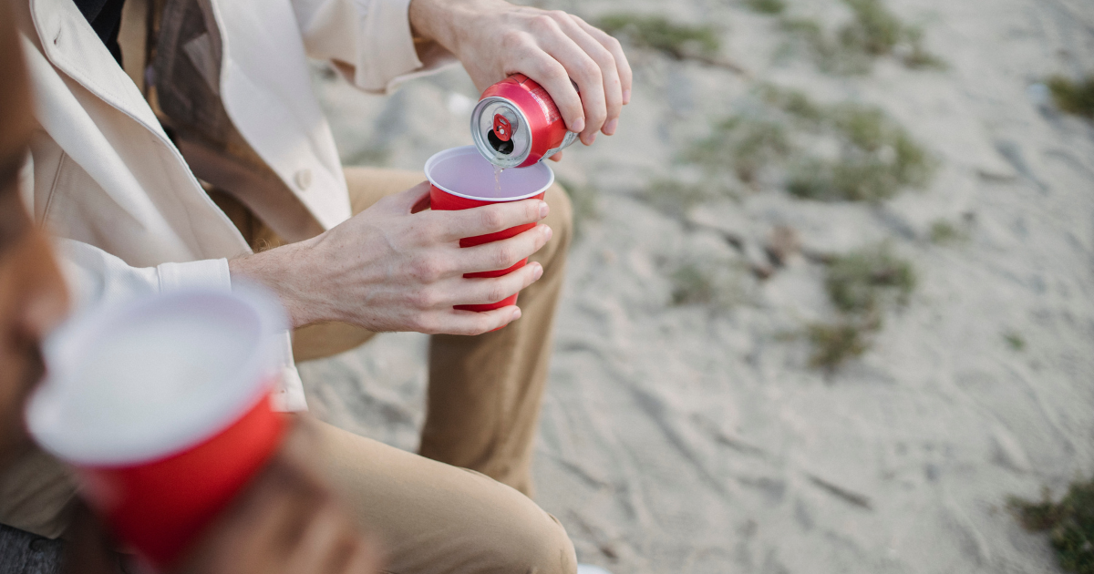 Person pouring a drink from a beverage can into a red cup while outdoors